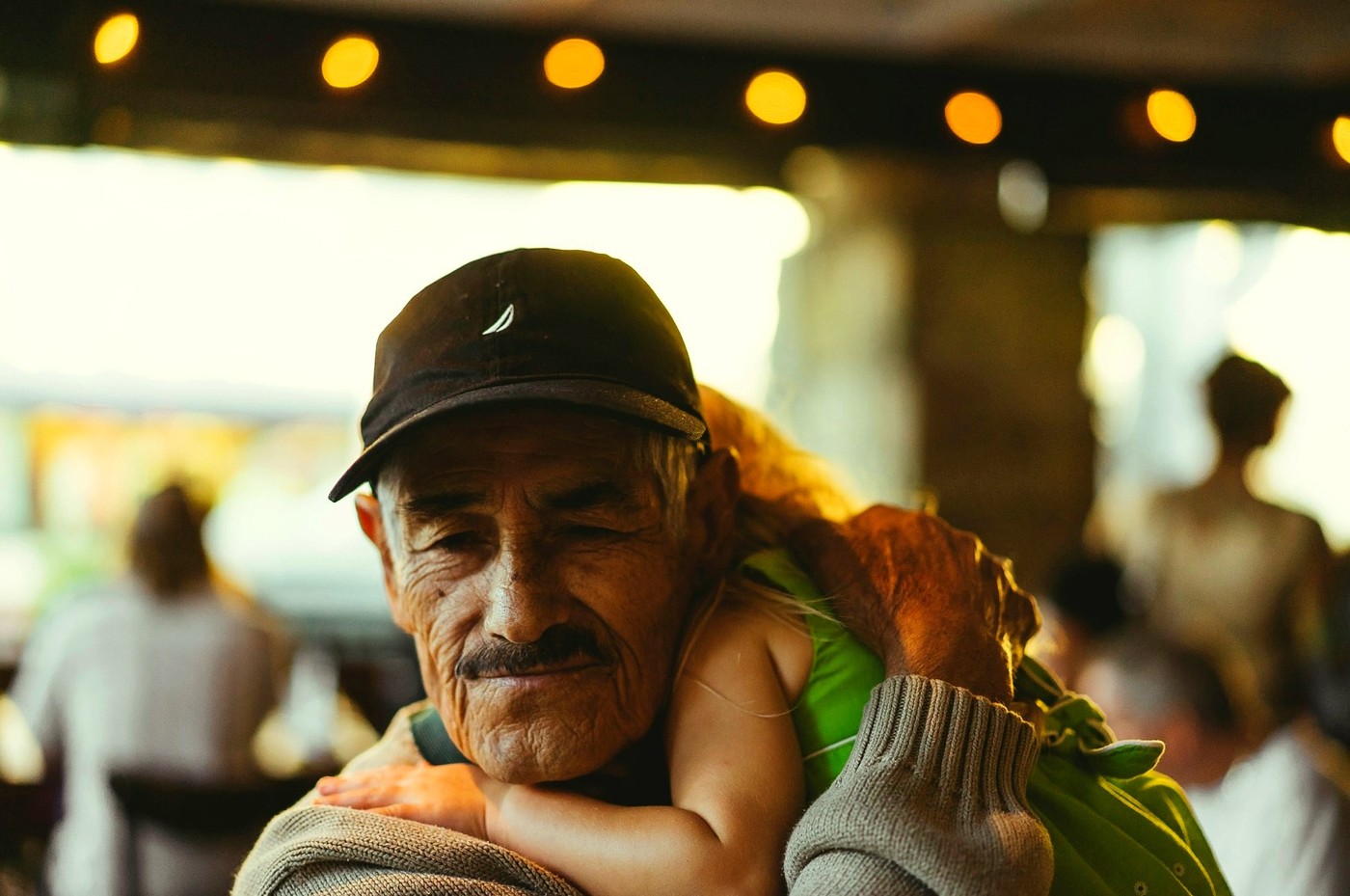 Un abuelo carga a su nieta sobre los hombros, luces cálidas de fondo